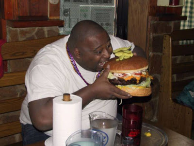 a photo of a large man eating the worlds largest cheeseburger.
